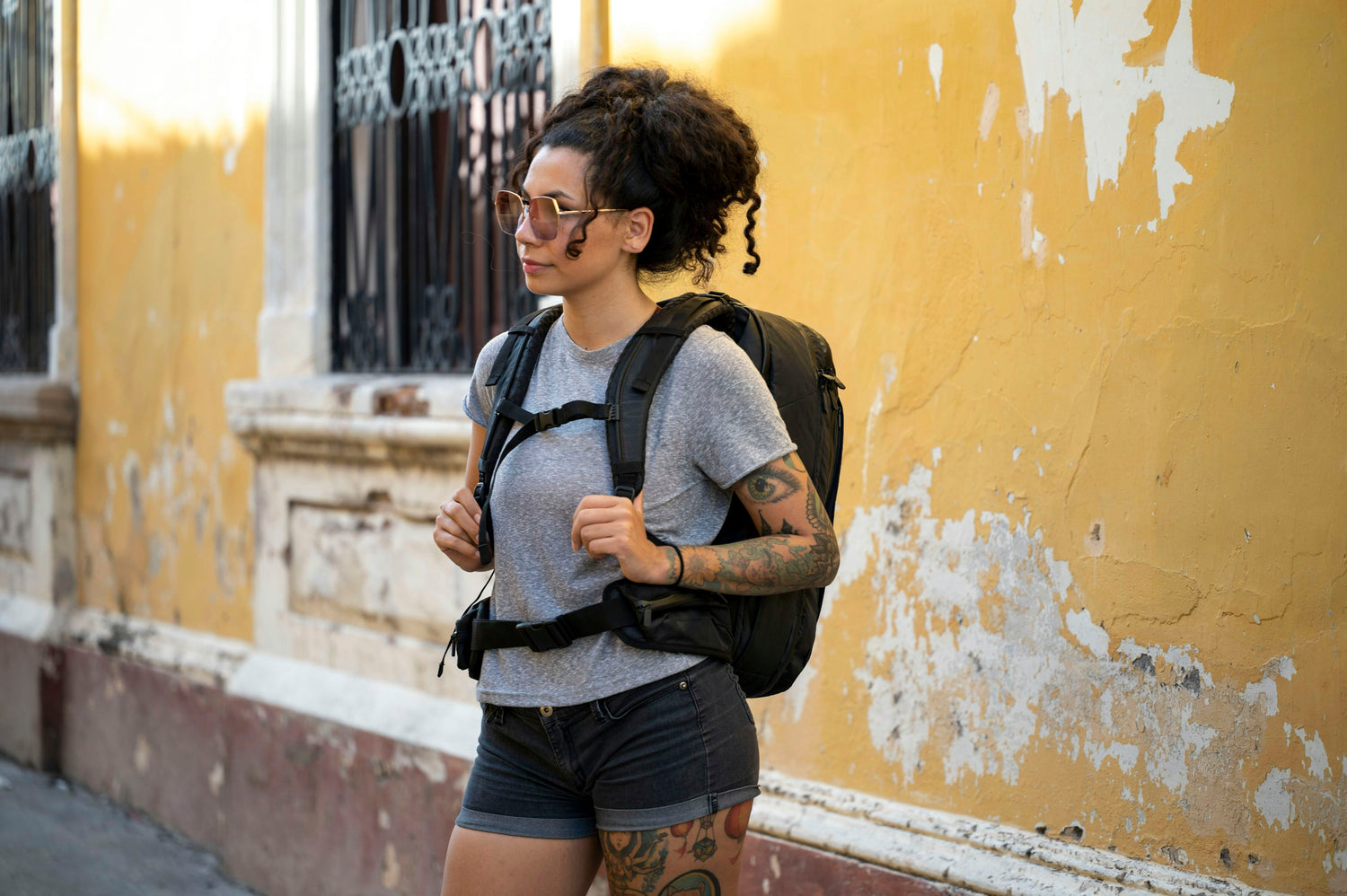 Woman wearing a Tortuga travel backpack in front of a faded yellow wall